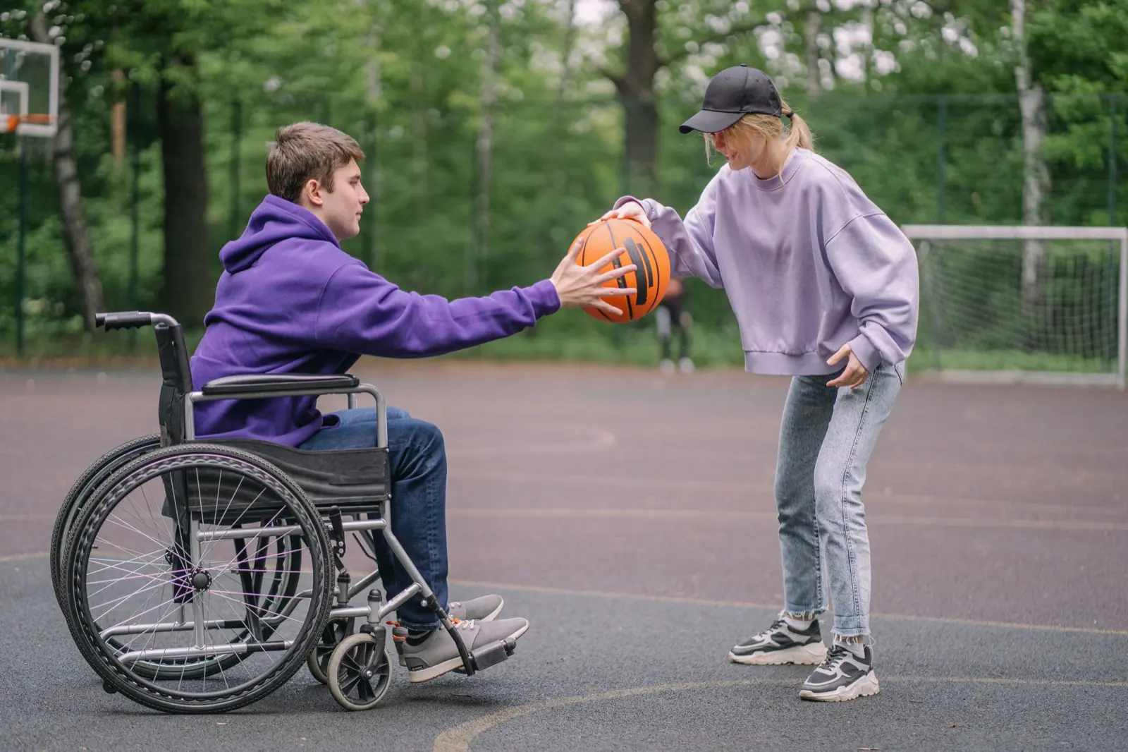 Two people playing basketball on an outdoor court, one of them using a wheelchair.