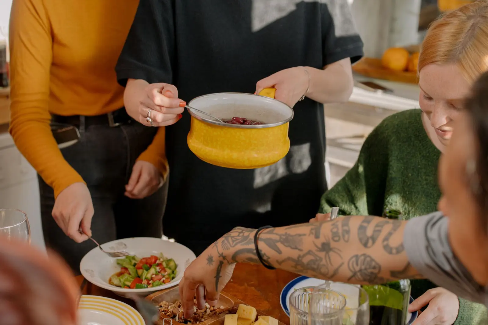 Housemates serving a shared meal together around a bright kitchen table.