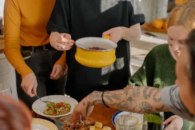 Housemates serving a shared meal together around a kitchen table.
