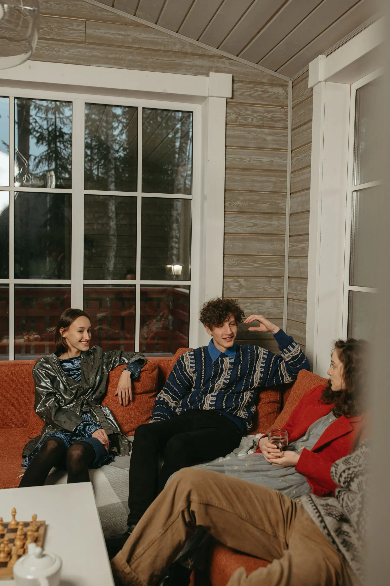Two people talking in a warm, window-lit lounge room of a shared home.